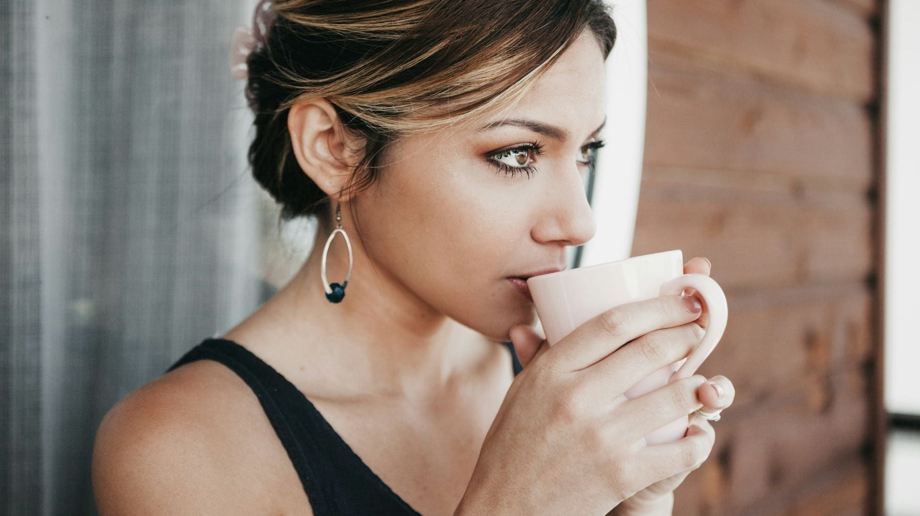 Woman sipping tea from a mug near a window