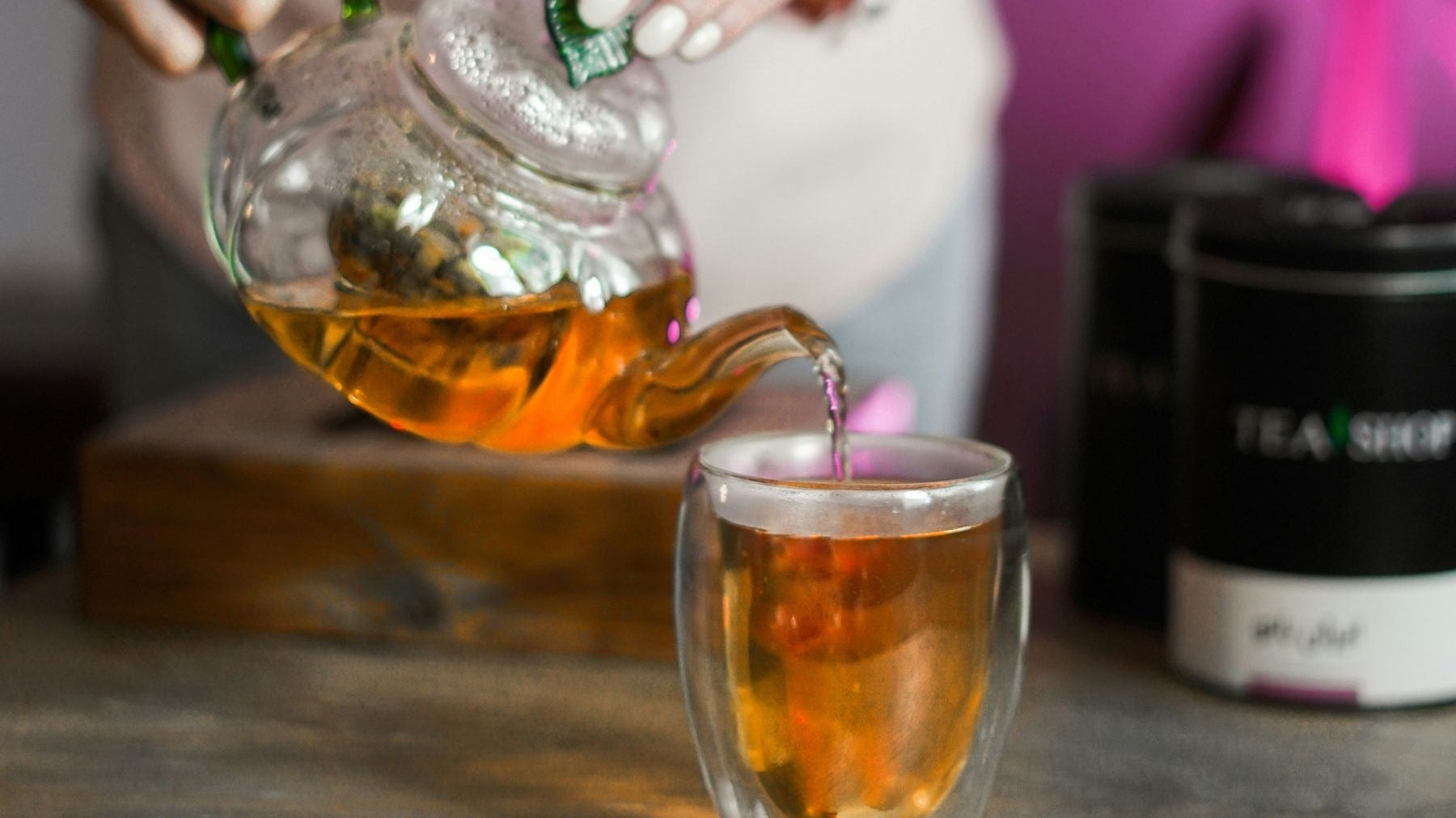 Tea being poured from a glass teapot into a clear cup.