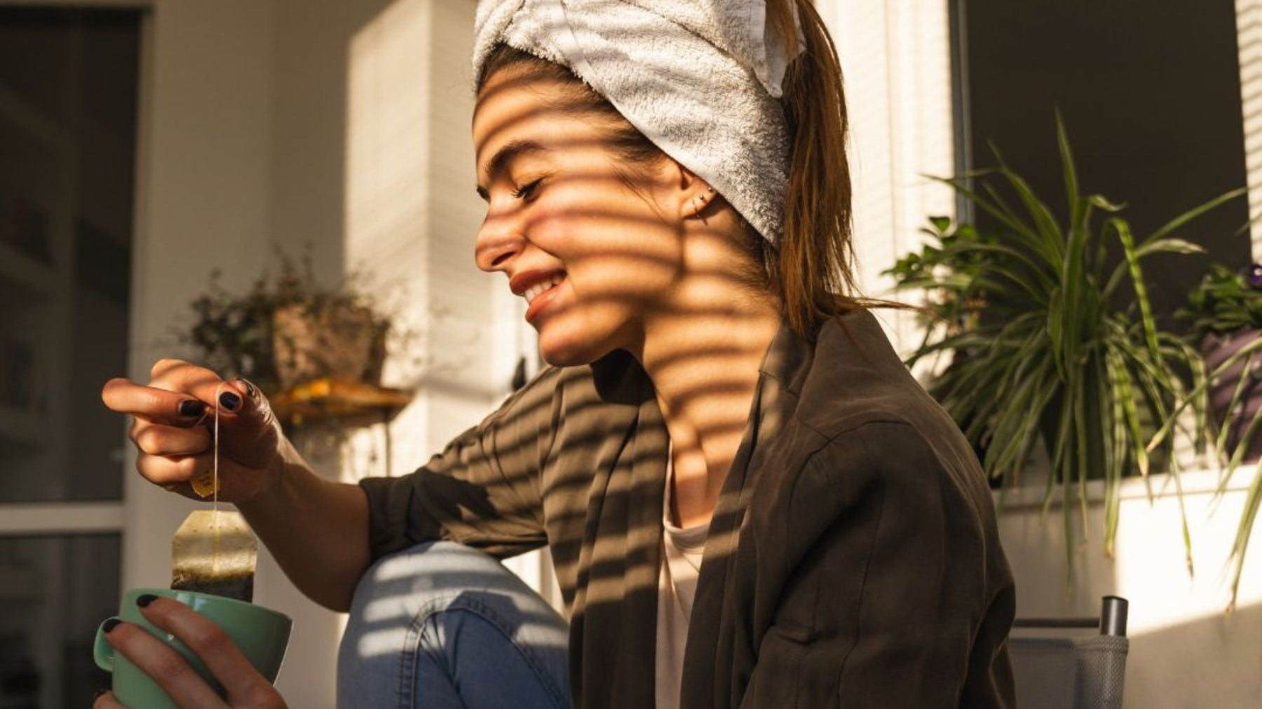 Woman smiling while dipping a tea bag into a mug in warm sunlight