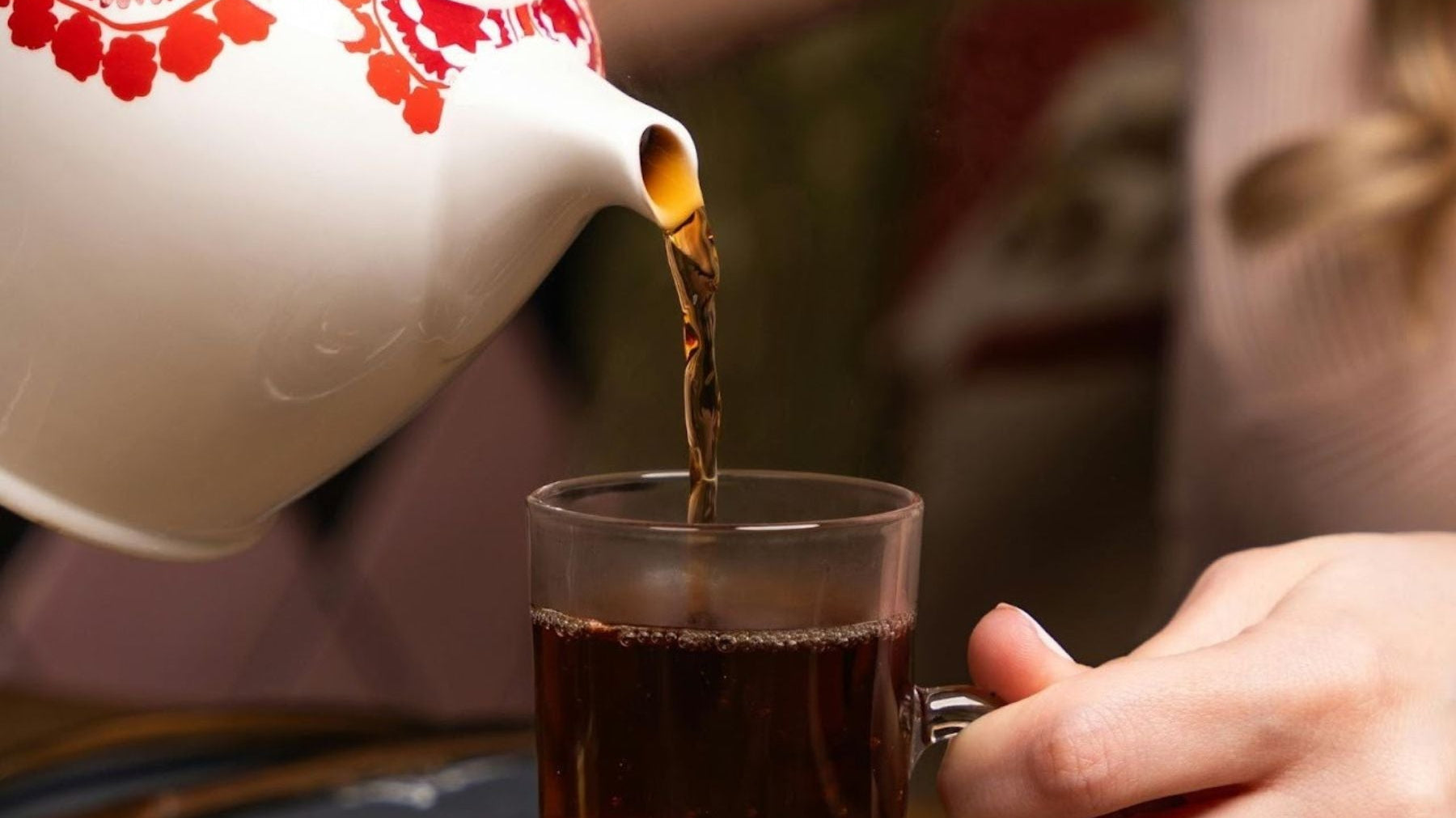 Black Tea being poured into a glass cup from a white kettle