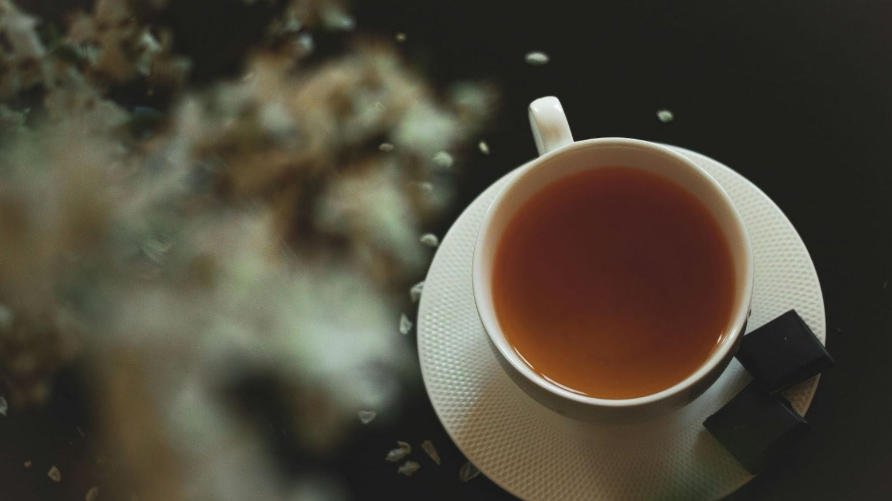 Cup of tea on a saucer with sugar cubes on a dark surface