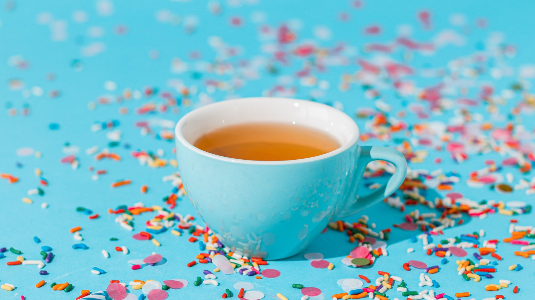 Blue cup of tea surrounded by colorful sprinkles on a bright blue background
