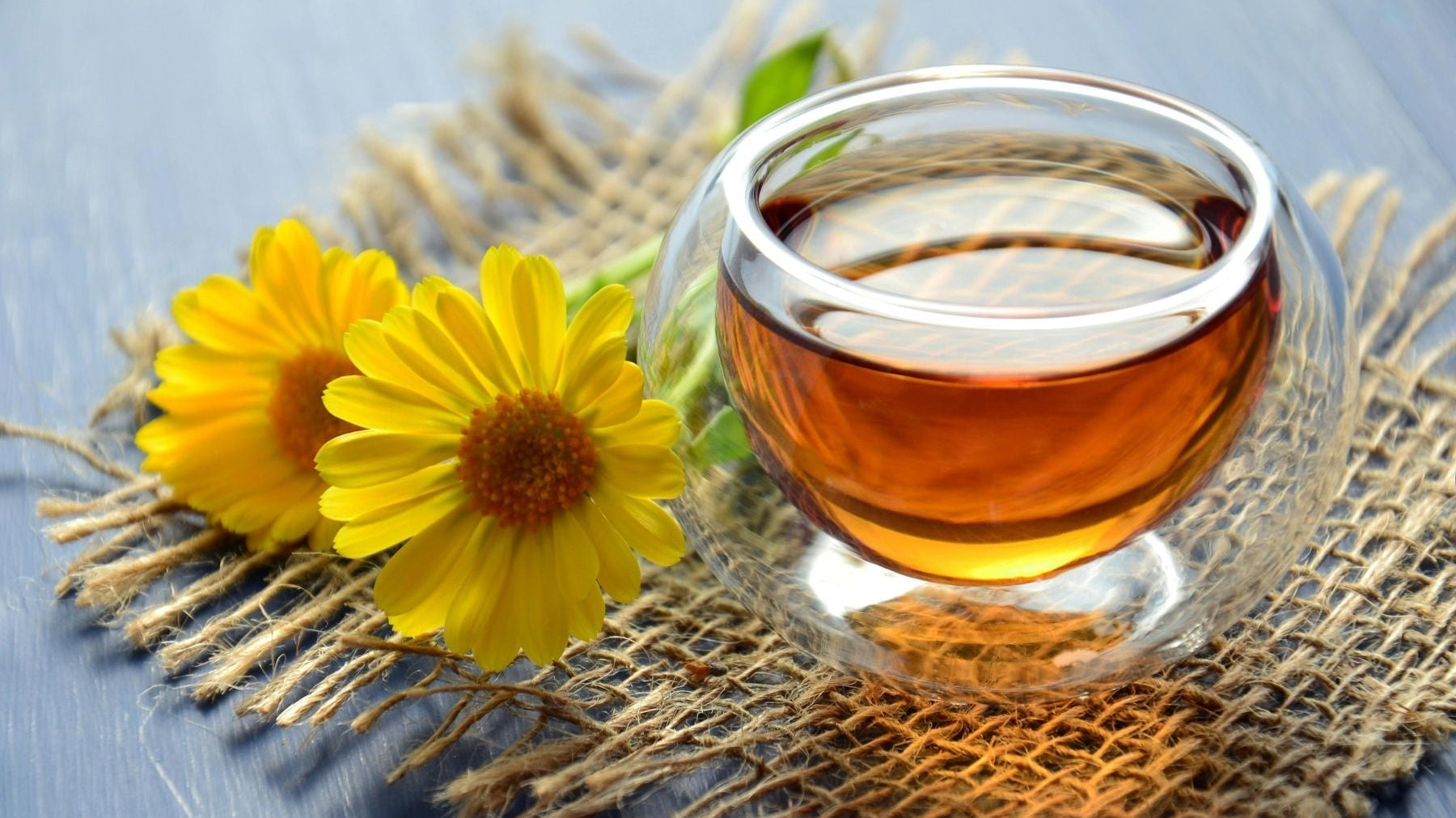 Glass cup of tea with yellow flowers on a rustic mat surface