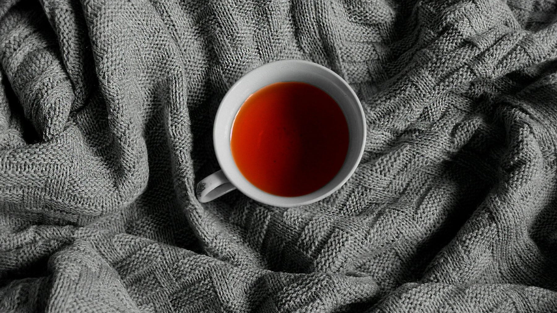 White cup of tea on a textured gray blanket