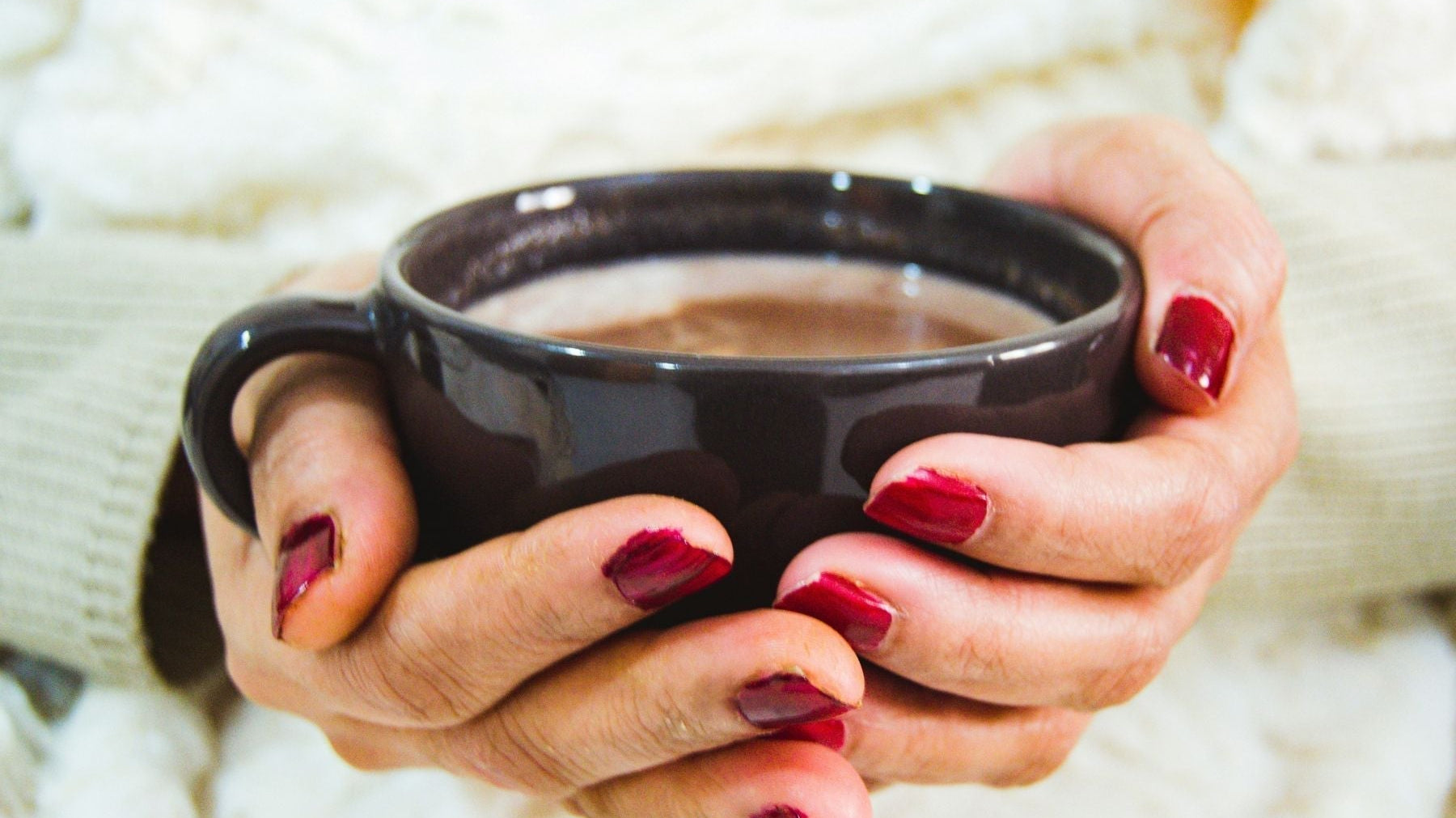 Hands holding a black mug of hot tea
