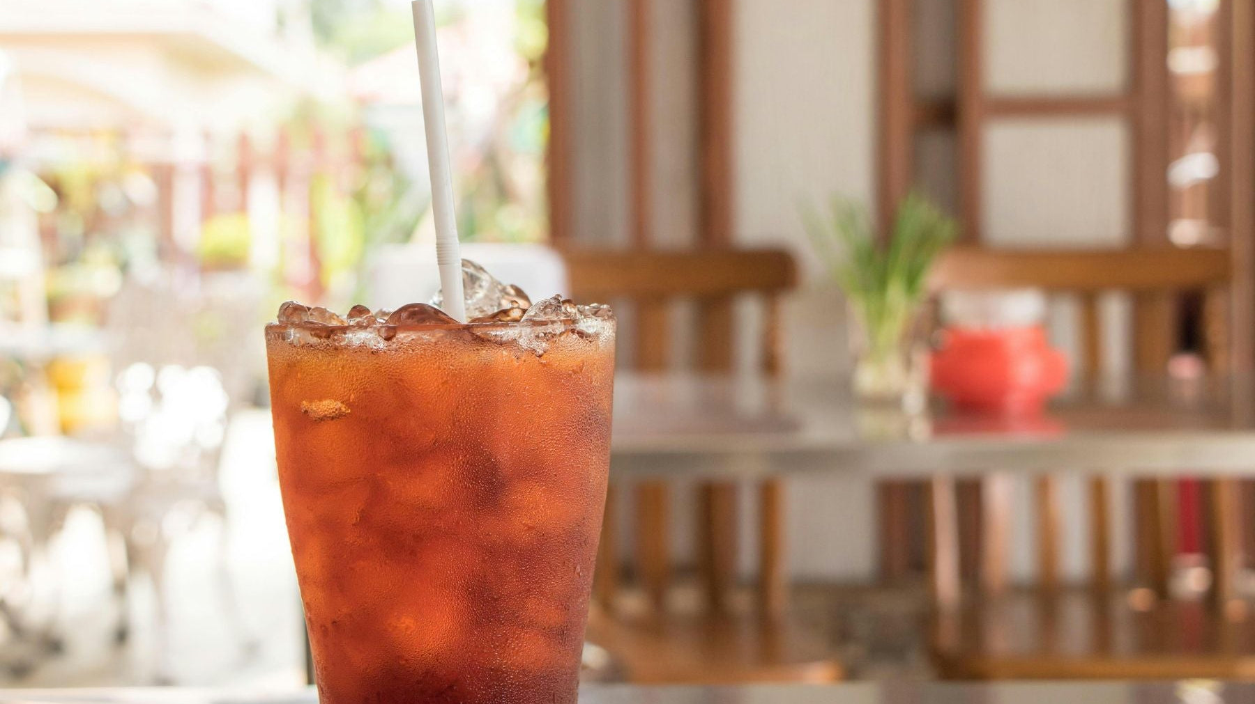 Glass of Peach Cobbler Iced Tea with straw and ice on a sunlit café table