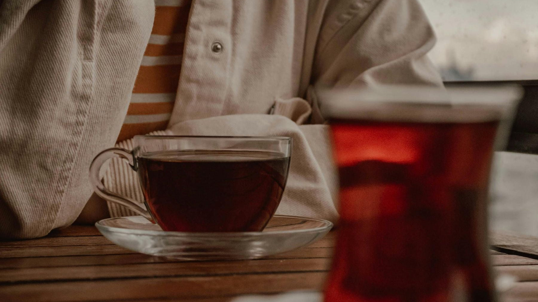 Person holding a glass cup of tea on a cozy table setting
