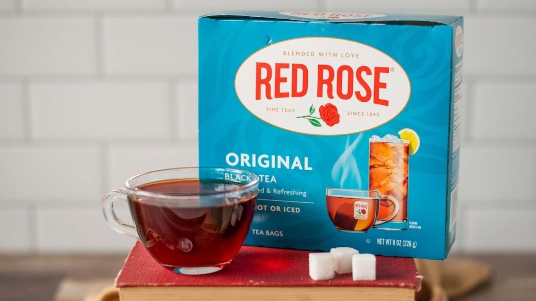 Red Rose original black tea box with cup and sugar cubes on stacked books