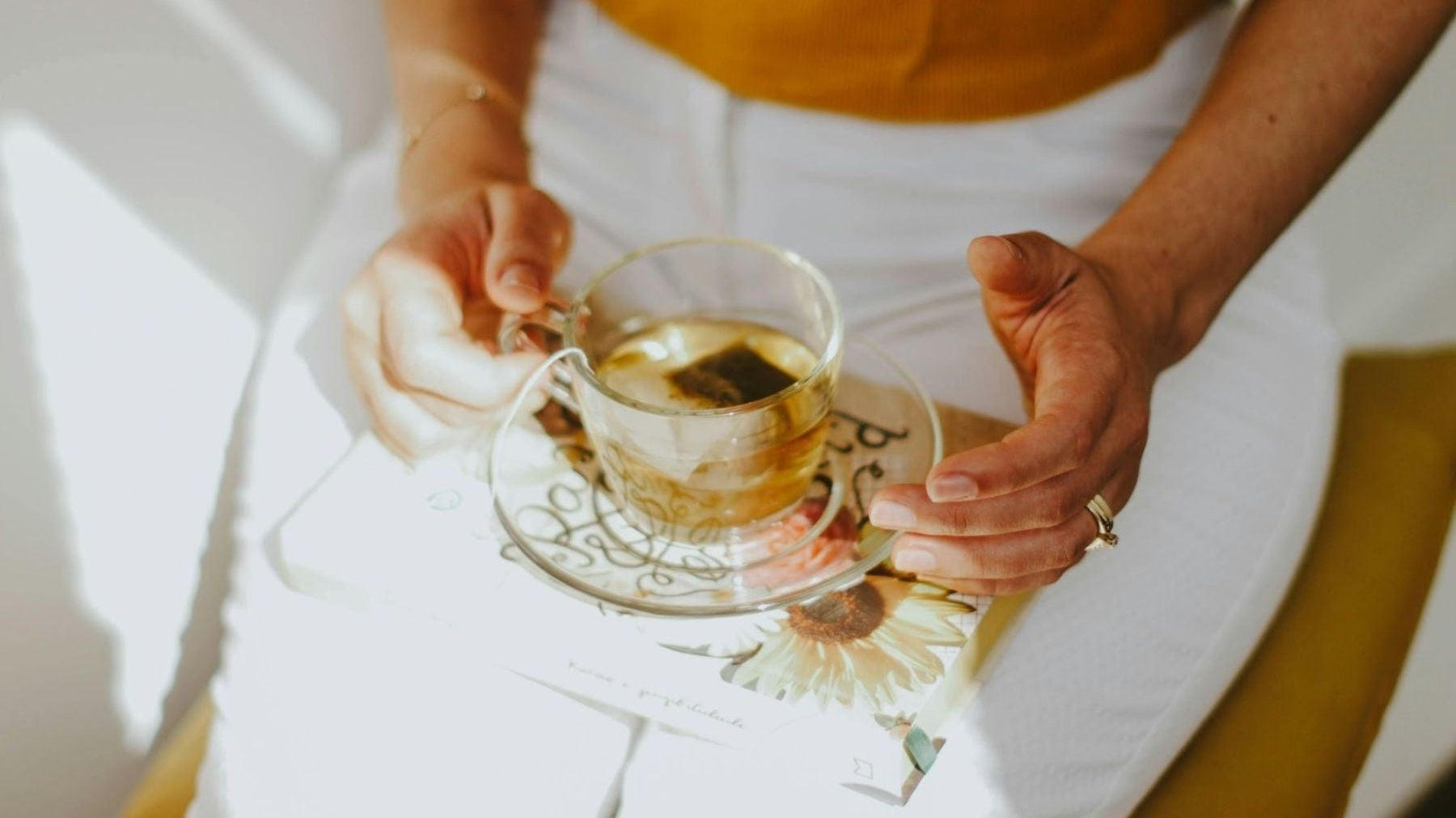 Close-up of hands holding a glass cup of tea over a book in natural sunlight