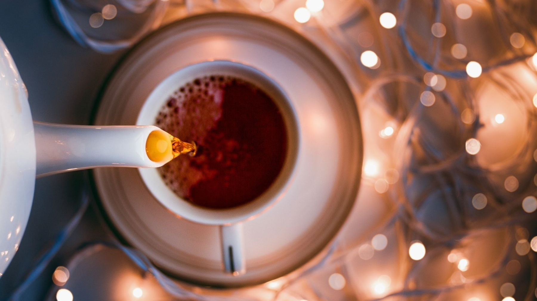 Overhead view of tea pouring into a cup surrounded by glowing fairy lights.