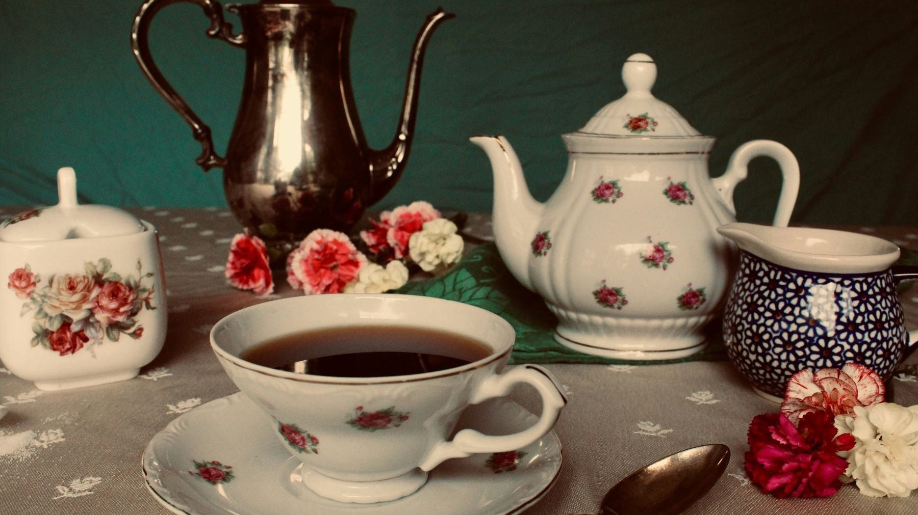 Vintage silver and floral china tea set arranged with a cup of black tea.