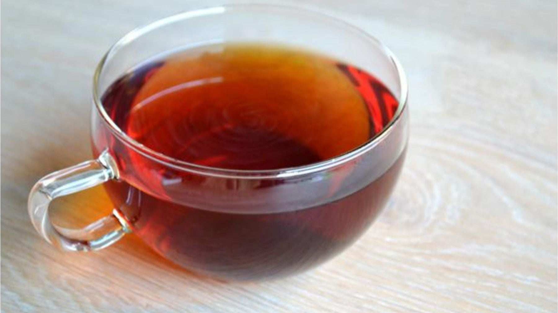 Clear glass cup filled with hot earl grey tea on a wooden table.