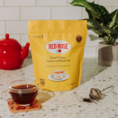 Yellow package of Red Rose Earl Grey loose leaf black tea on a kitchen counter with a cup of tea and red teapot.