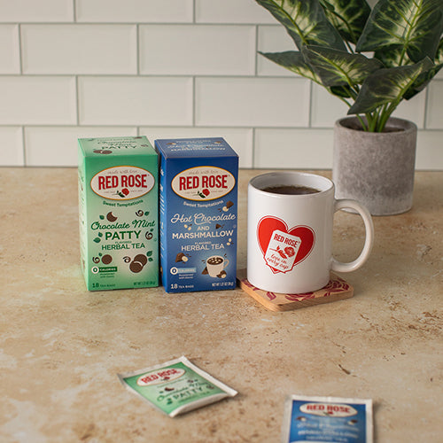 Red Rose tea boxes and a mug on a kitchen counter with a plant in the background.