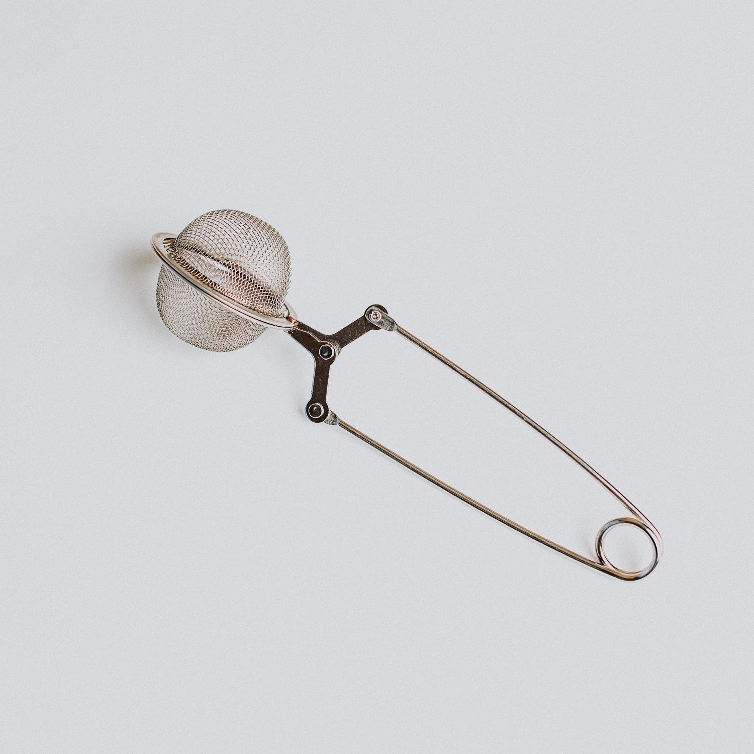 A close-up, top-down view of a silver, stainless steel mesh tea ball infuser with a long handle