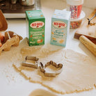 A set of cookie cutters shaped like cookies and tea cups laid out on a table with rolled out dough, with boxes of Red Rose Gingerbread Cookie and Sugar Cookie teas in the background.