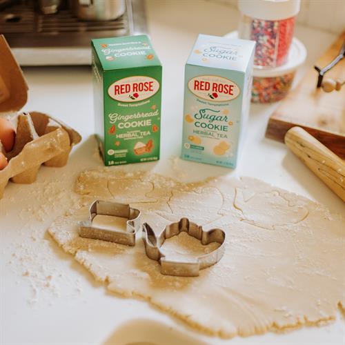 A set of cookie cutters shaped like cookies and tea cups laid out on a table with rolled out dough, with boxes of Red Rose Gingerbread Cookie and Sugar Cookie teas in the background.