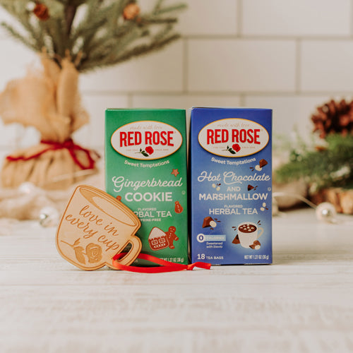 Packaging of Red Rose Sweet Temptations Herbal Tea varieties, including Hot Chocolate and Marshmallow, and Gingerbread Cookie flavors, along with a holiday ornament.