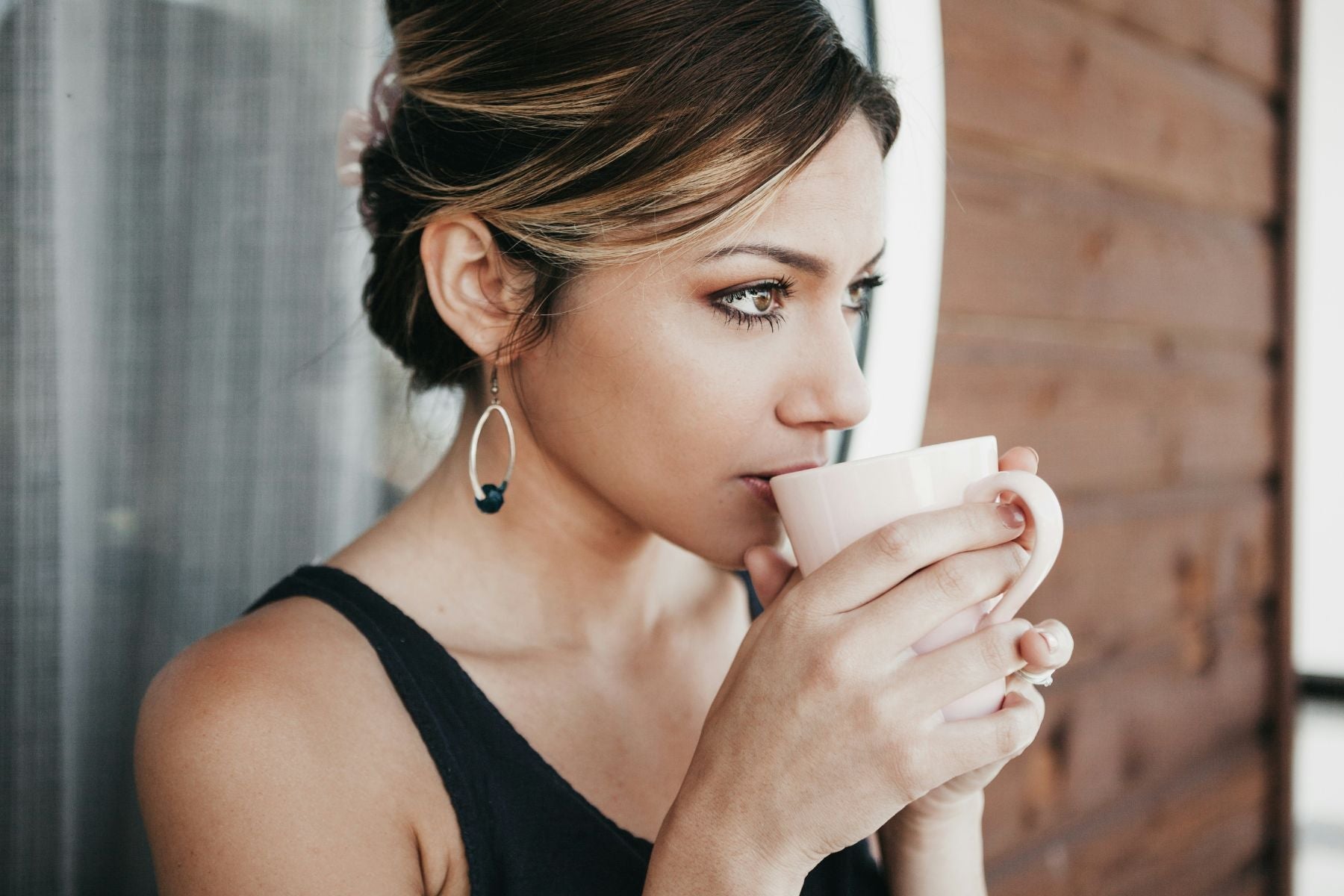 Woman sipping tea from a mug near a window