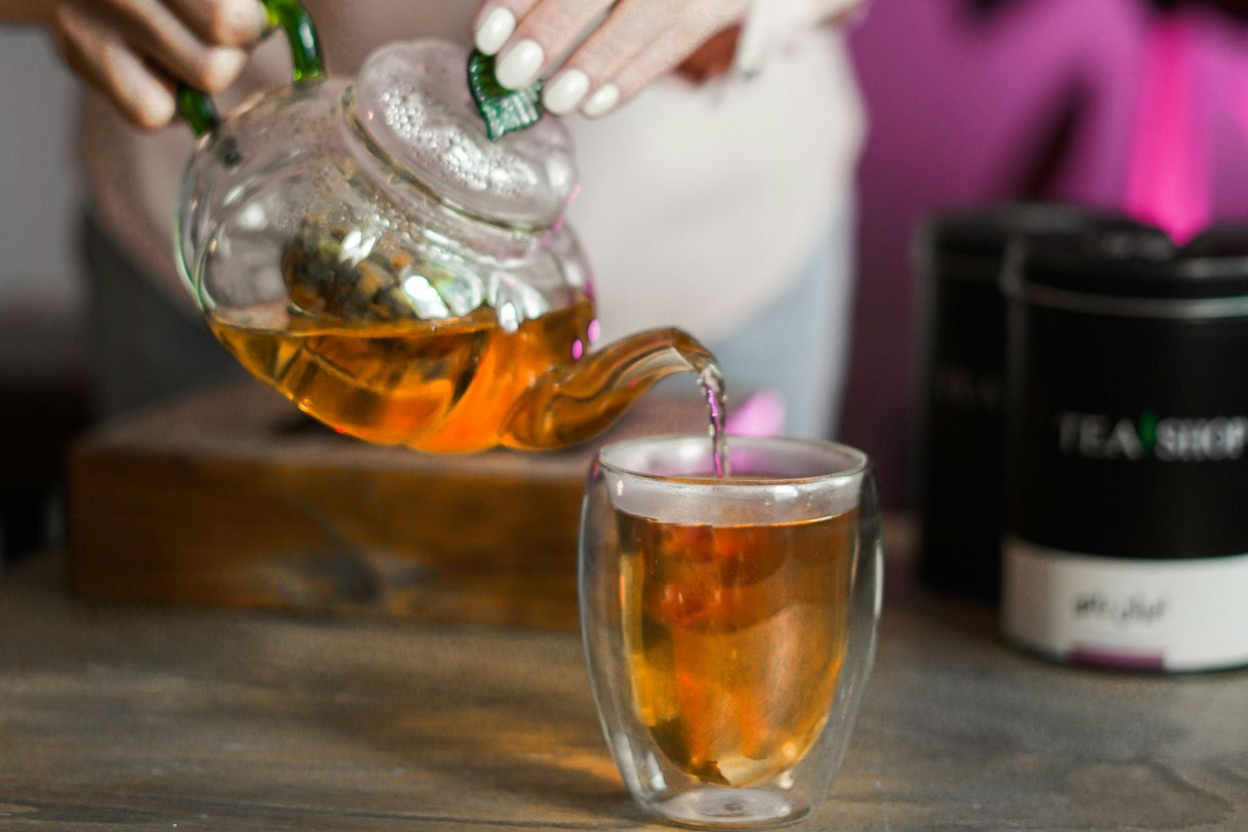 Tea being poured from a glass teapot into a clear cup.