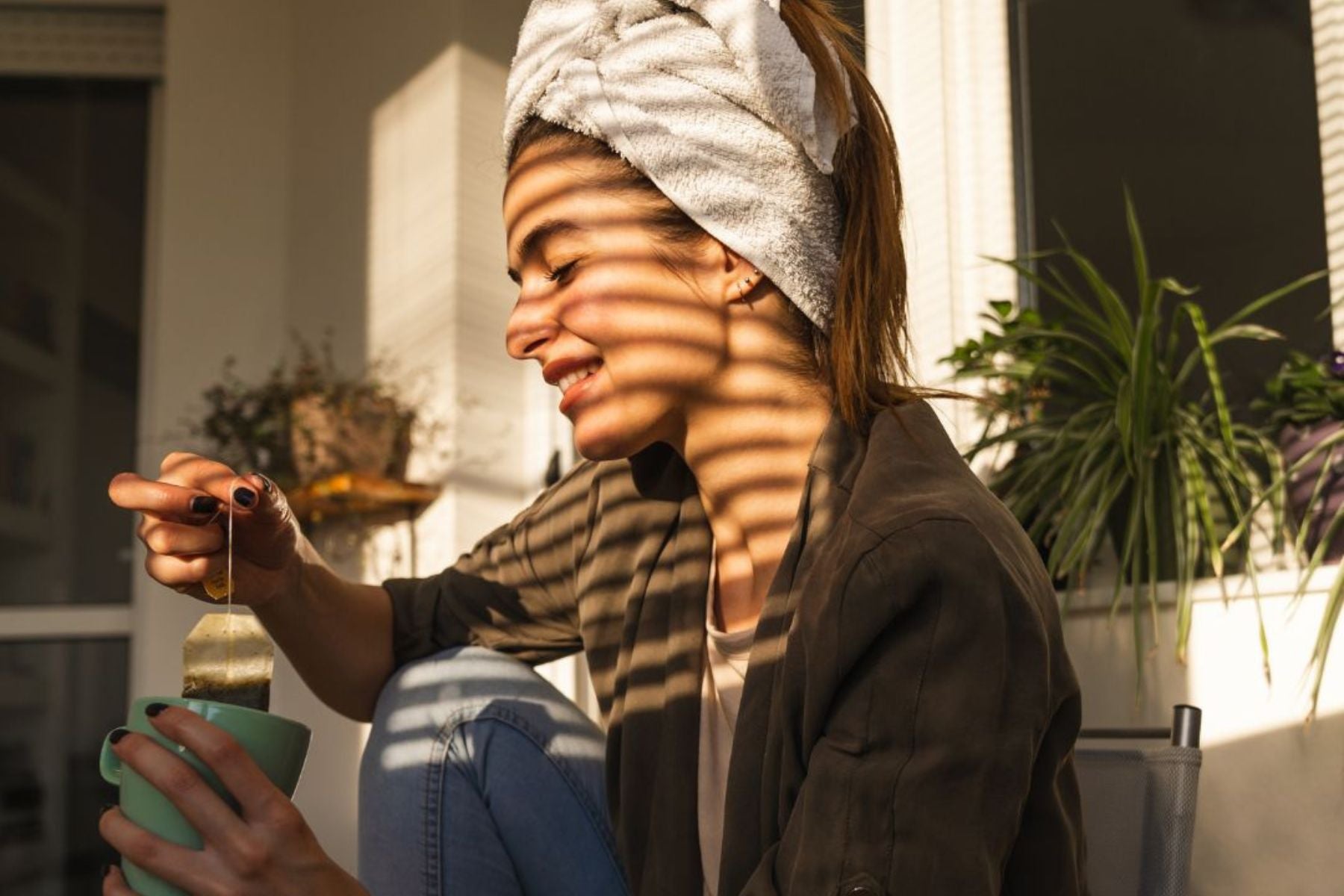 Woman smiling while dipping a tea bag into a mug in warm sunlight