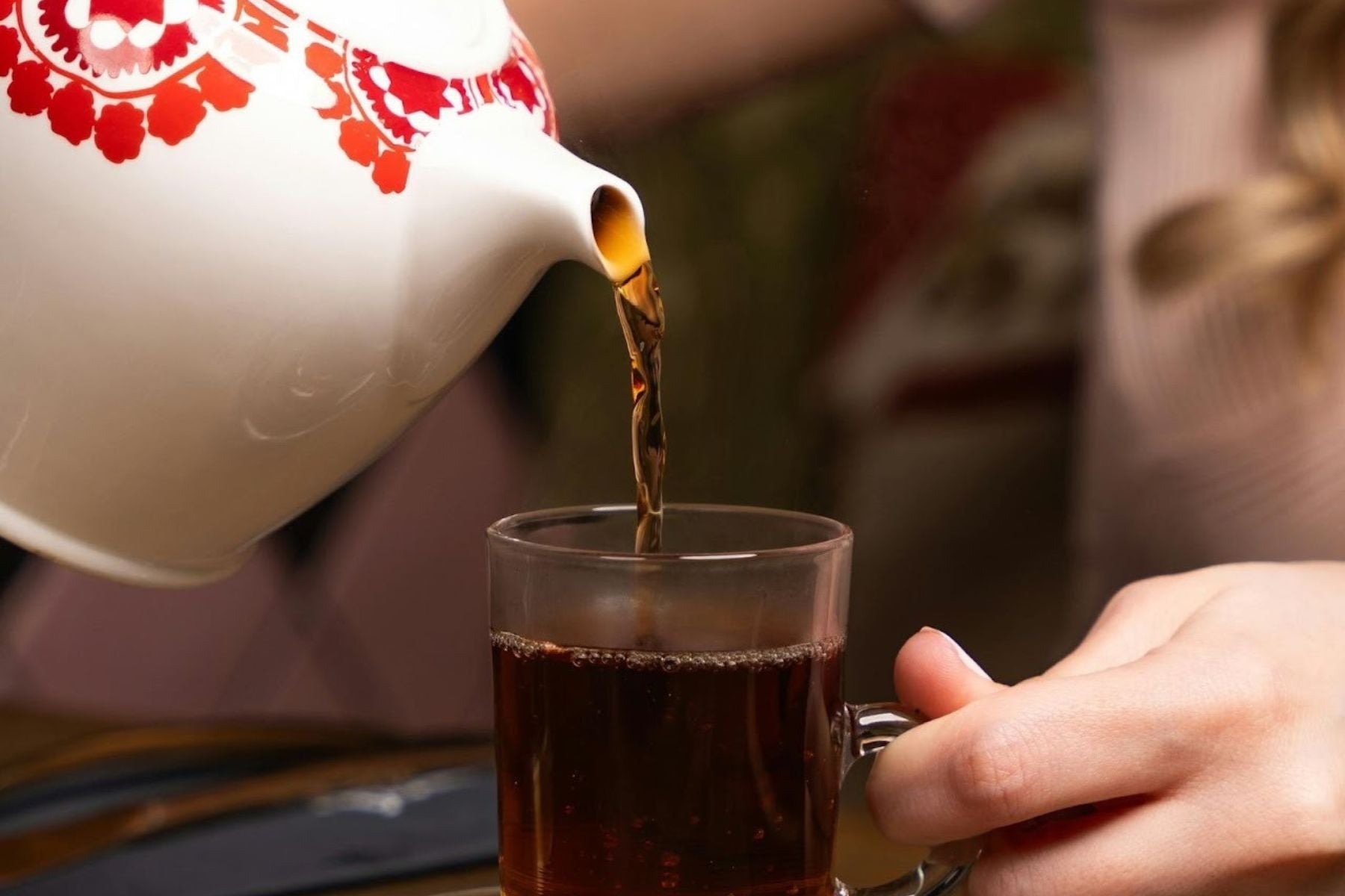 Black Tea being poured into a glass cup from a white kettle