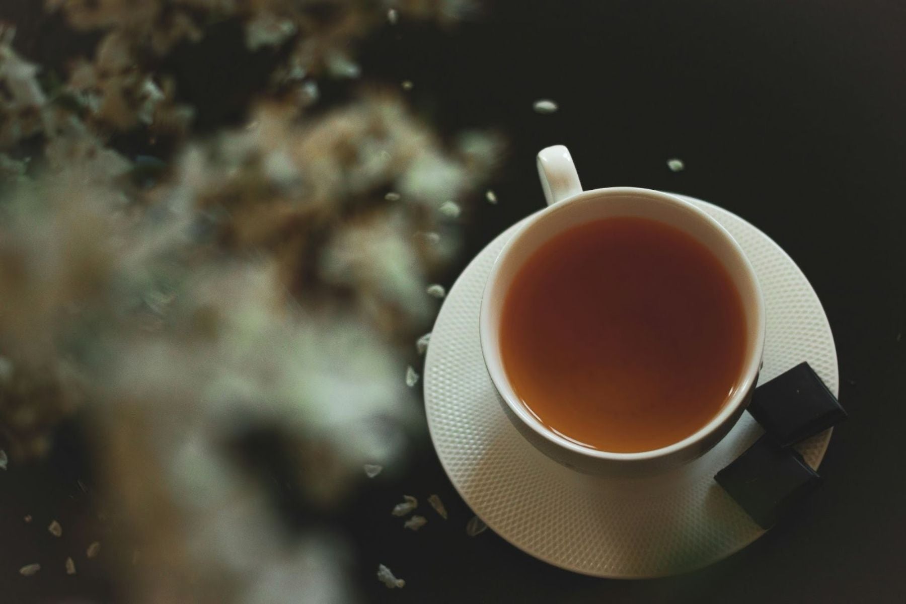 Cup of tea on a saucer with sugar cubes on a dark surface