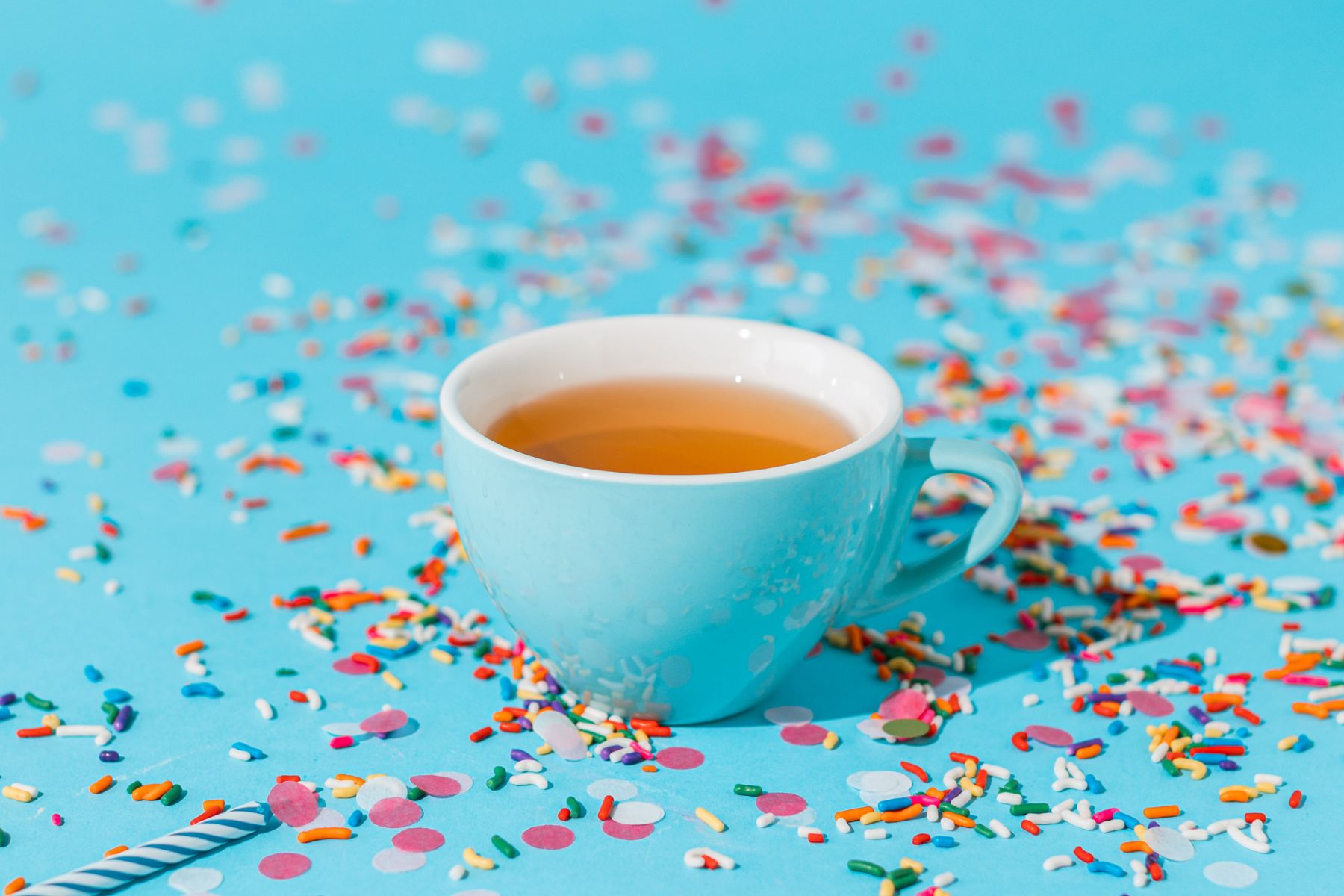 Blue cup of tea surrounded by colorful sprinkles on a bright blue background