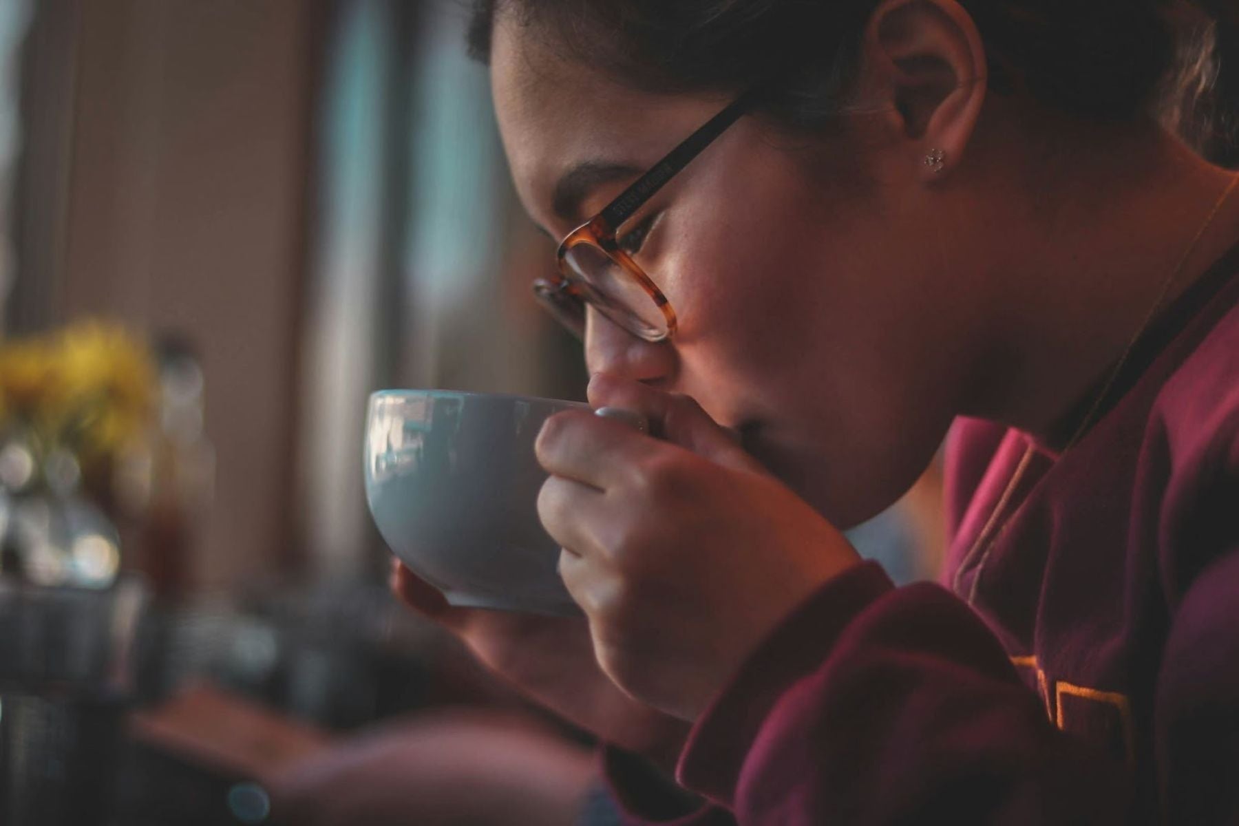 Person wearing glasses sipping tea from a cup in a softly lit setting