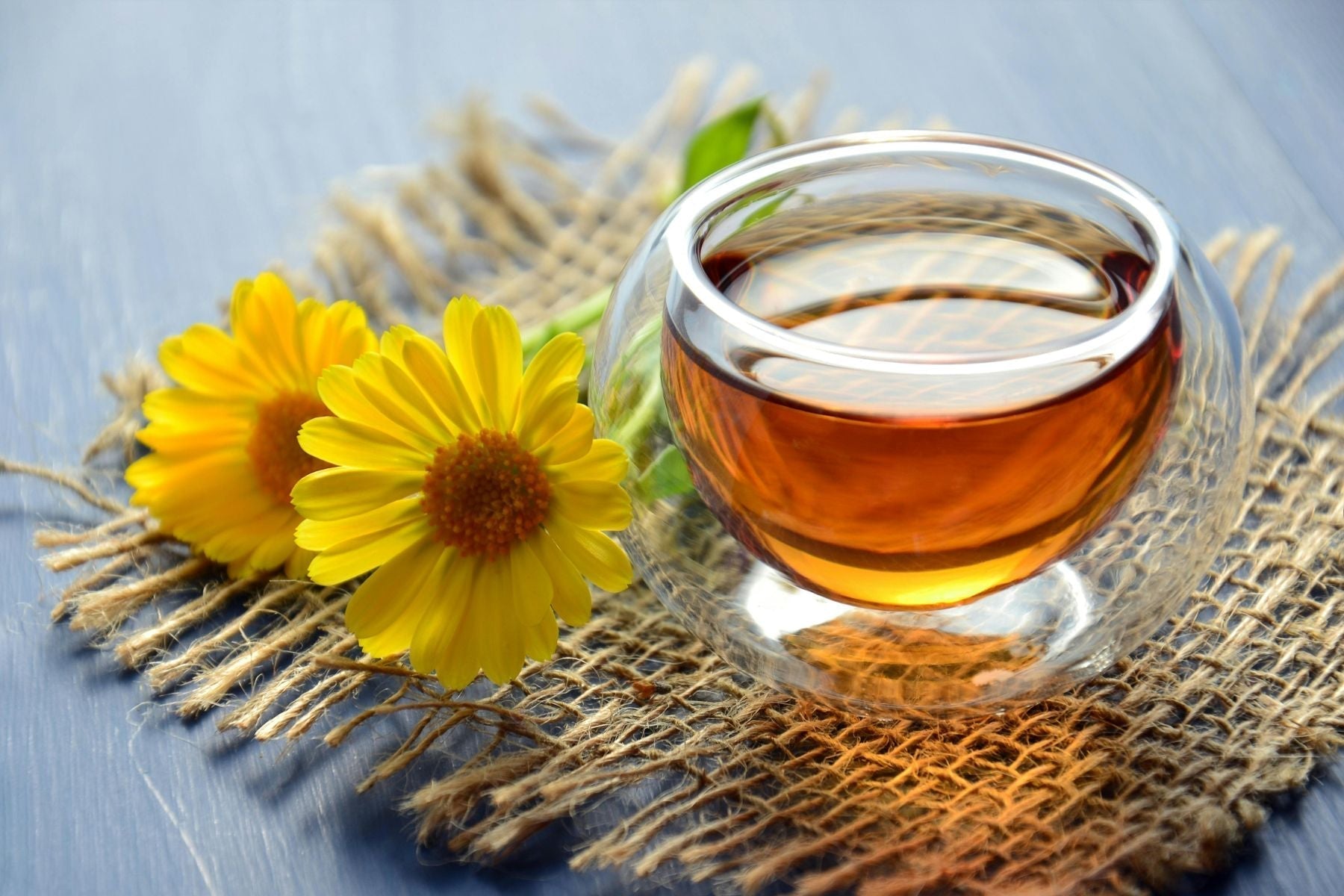 Glass cup of tea with yellow flowers on a rustic mat surface