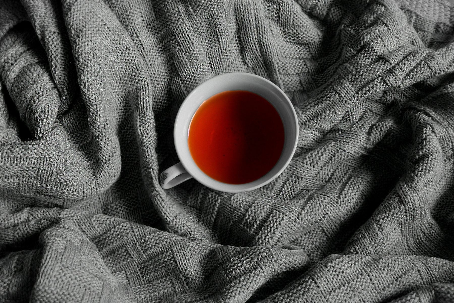 White cup of tea on a textured gray blanket