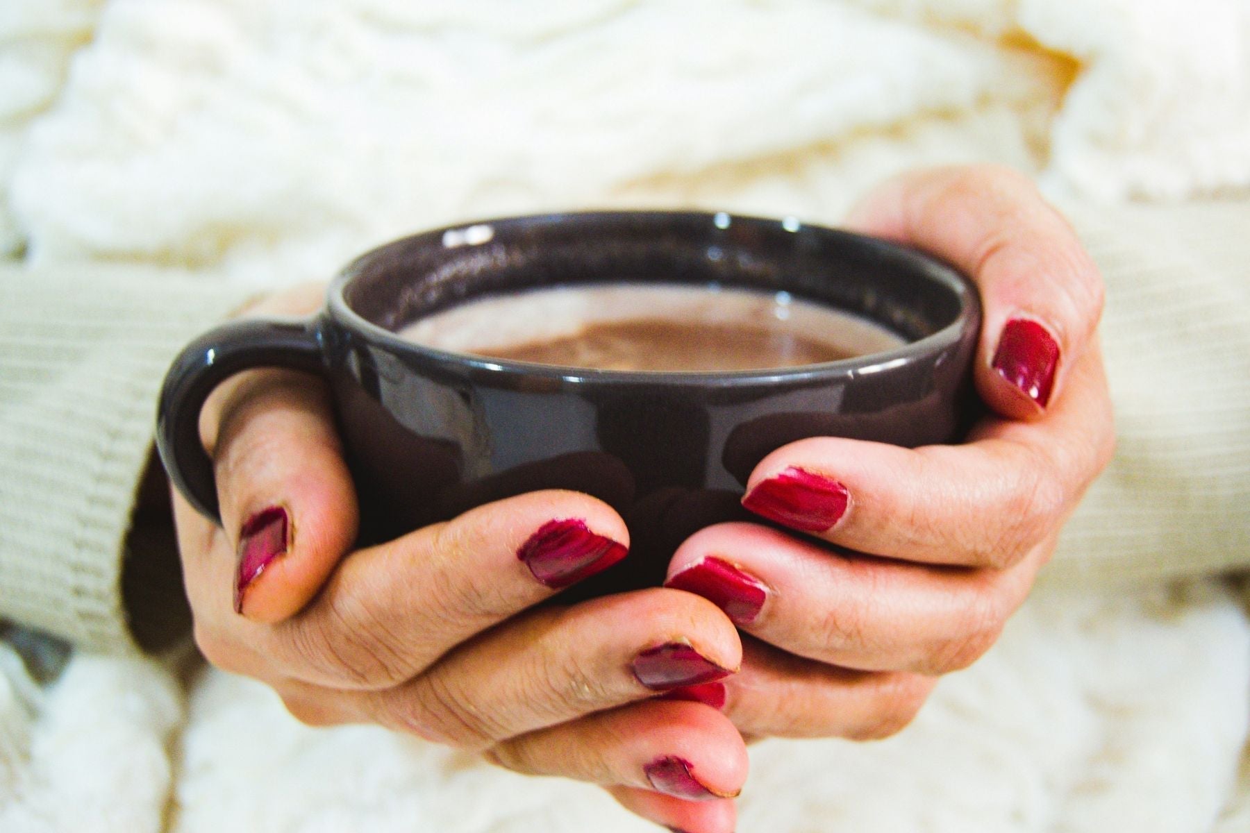Hands holding a black mug of hot tea