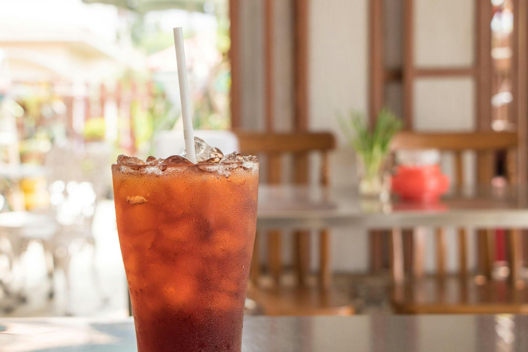 Glass of Peach Cobbler Iced Tea with straw and ice on a sunlit café table