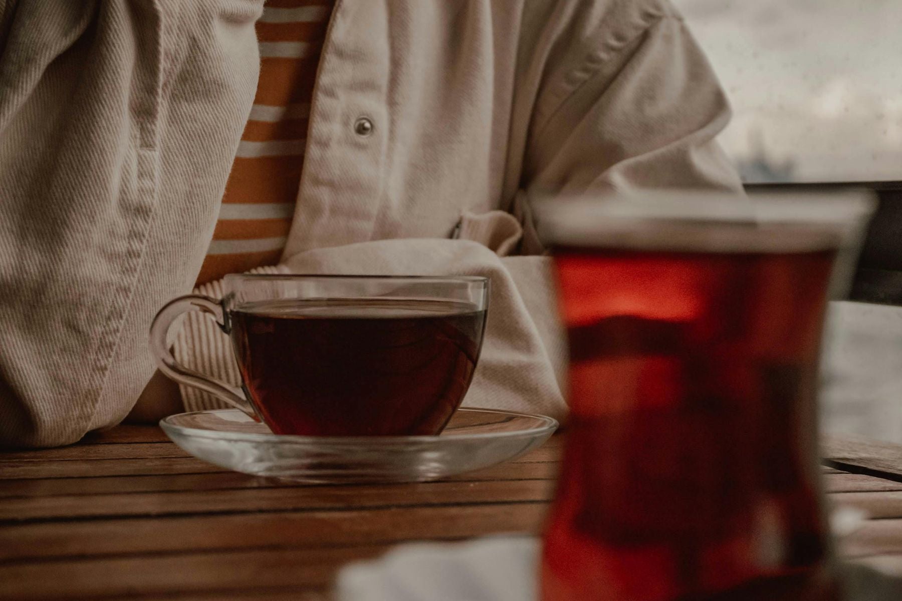 Person holding a glass cup of tea on a cozy table setting