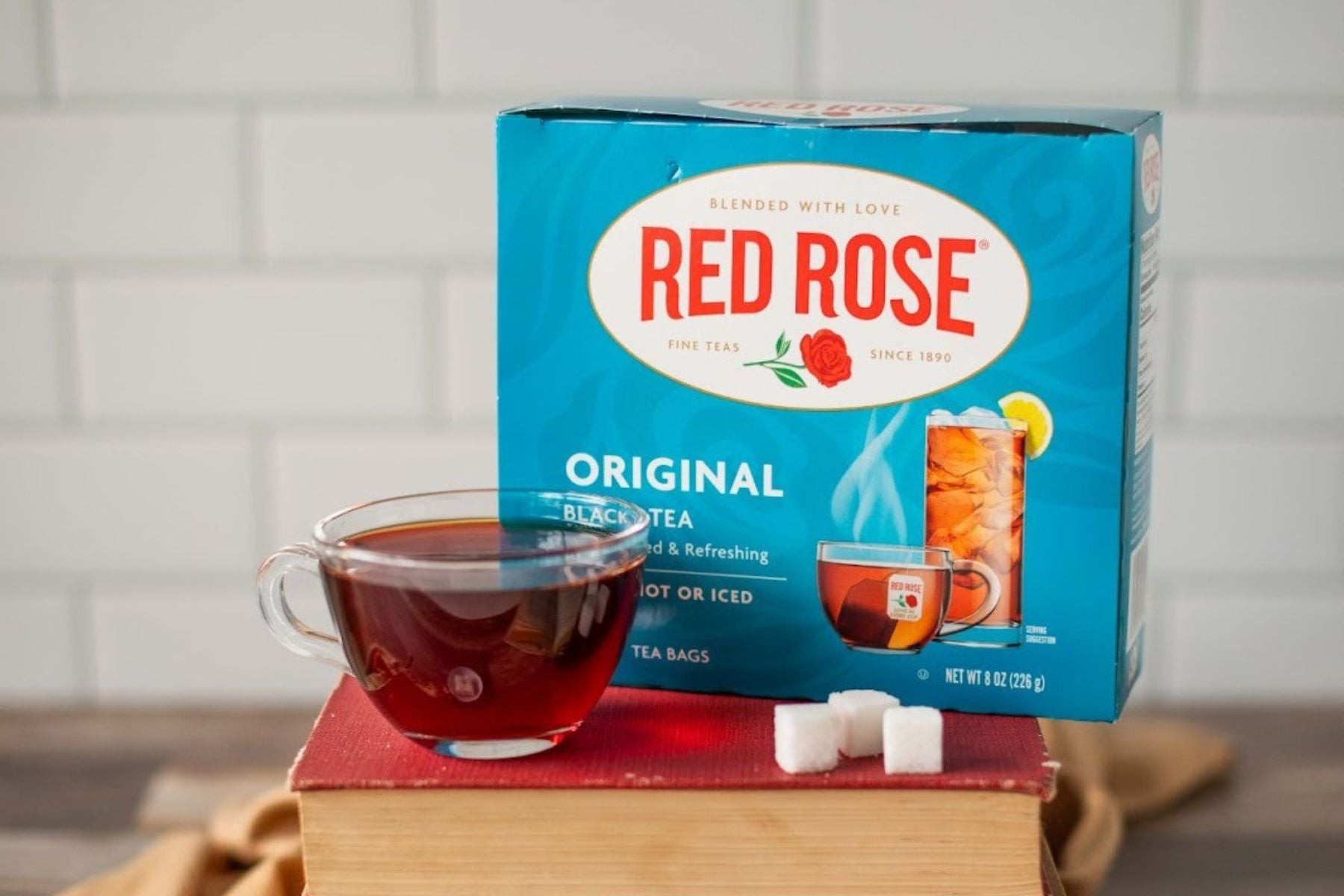 Red Rose original black tea box with cup and sugar cubes on stacked books
