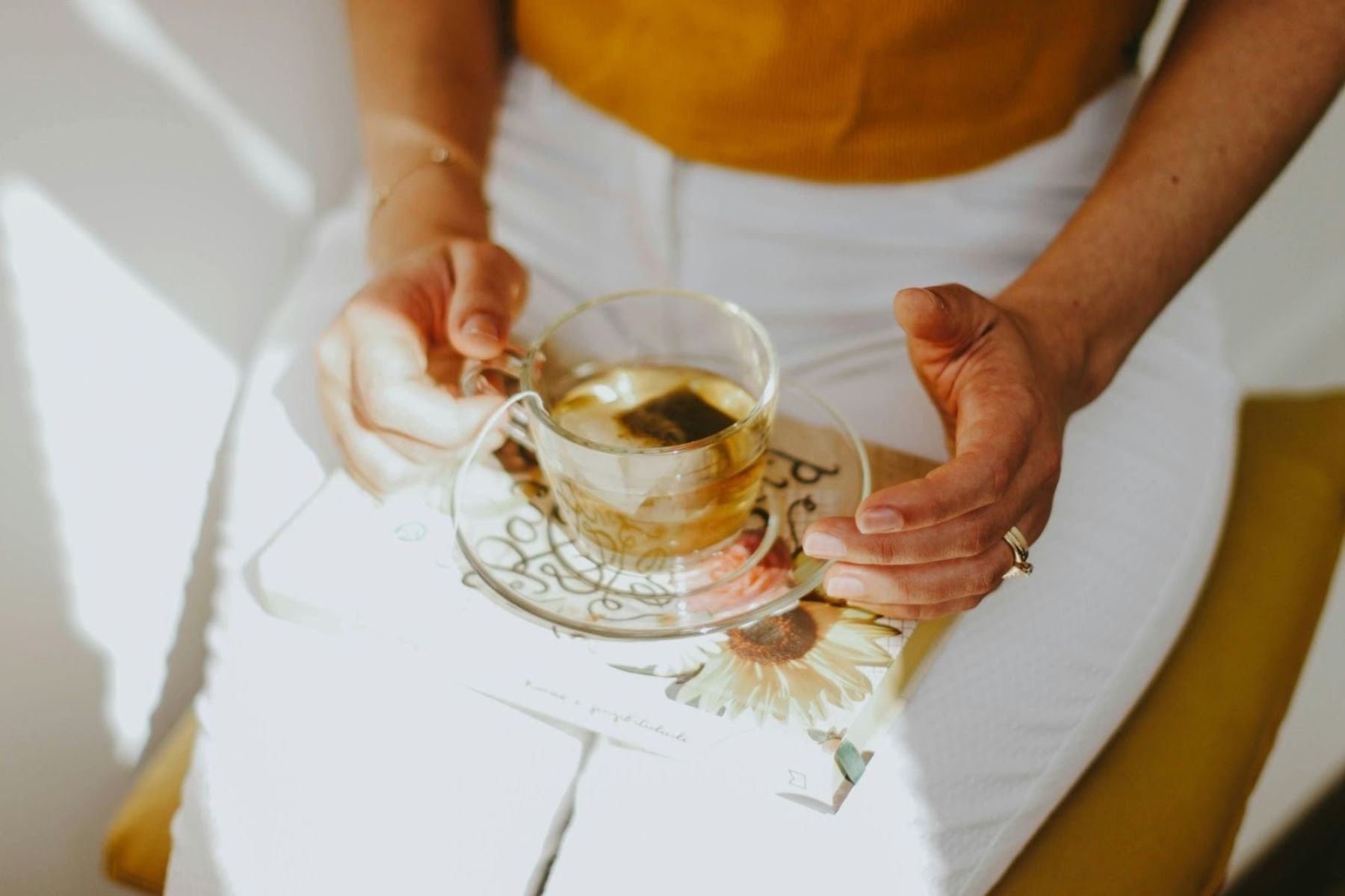 Close-up of hands holding a glass cup of tea over a book in natural sunlight