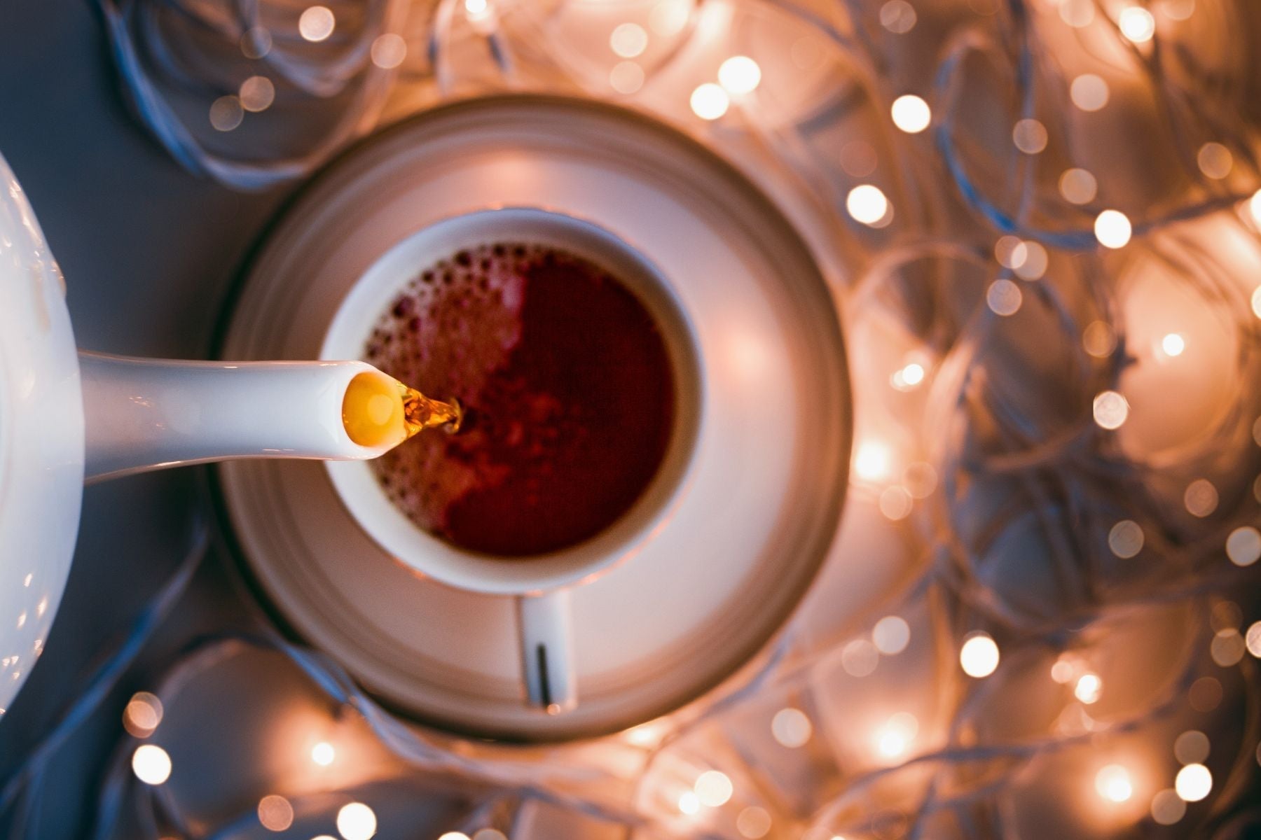 Overhead view of tea pouring into a cup surrounded by glowing fairy lights.