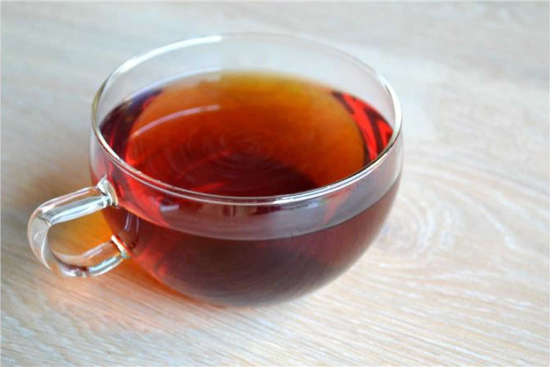 Clear glass cup filled with hot earl grey tea on a wooden table.