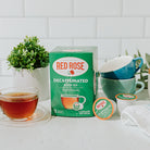 Red Rose Decaffeinated Black Tea Single Serve Cups packaging with a cup of tea and tea cups on a white surface.