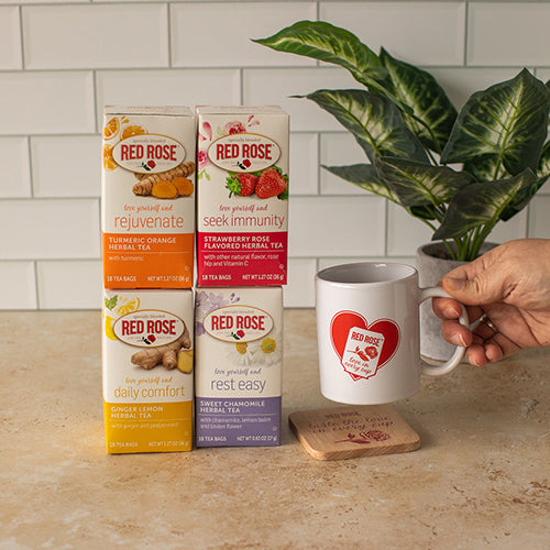 Red Rose herbal tea blend boxes with a mug and coaster and a plant in the background