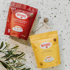 Two Red Rose tea packages, one red English Breakfast Loose Leaf and one yellow Earl Grey Loose Leaf, on a white background with a snapball style stainless steel infuser